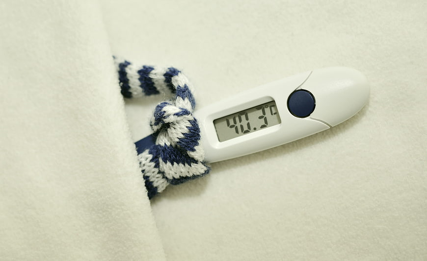 Digital thermometer showing high fever under white blanket