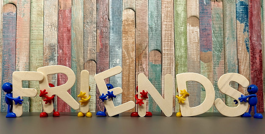 Colorful figures holding wooden letters spelling friends