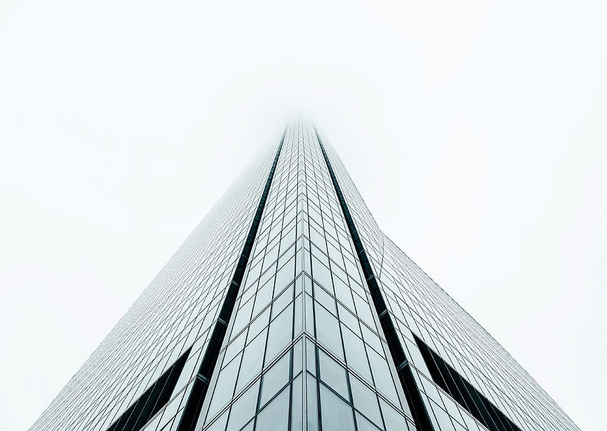 Low angle view of modern glass skyscraper disappearing into fog