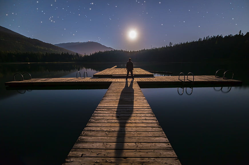 Silhouette of Man Standing on Wooden Dock Under Starry Night Sky