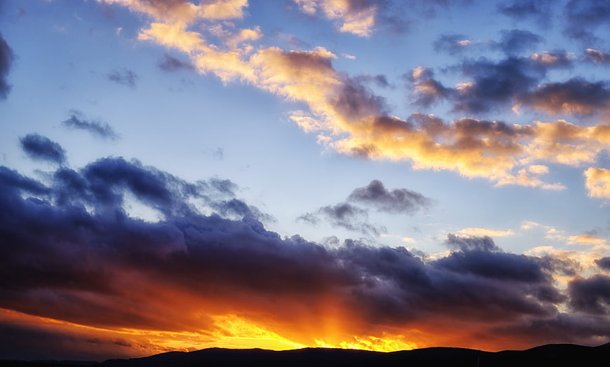 Dramatic sunset with golden sunbeams breaking through dark clouds