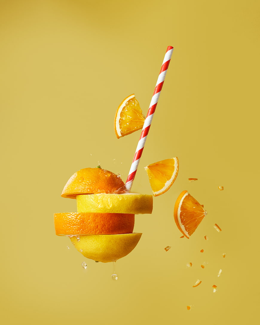 Fresh citrus fruit slices and straw floating on yellow background