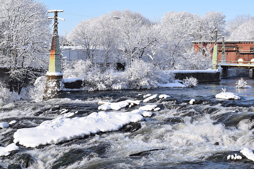 Snow-covered river rapids with industrial bridge and frosted trees