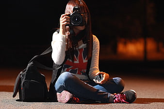 Young Woman Photographer Sitting on Street at Night with Camera