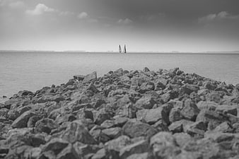 Black and white sailboats on calm sea with rocky foreground