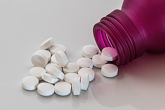 White Pills Spilling From Purple Bottle On White Surface