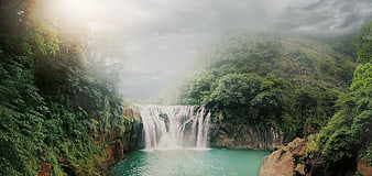 Misty Tropical Waterfall Cascading Into Turquoise Pool Surrounded By Lush Jungle