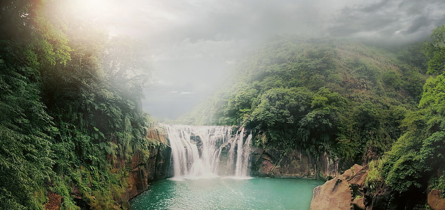 Misty Tropical Waterfall Cascading Into Turquoise Pool Surrounded By Lush Jungle