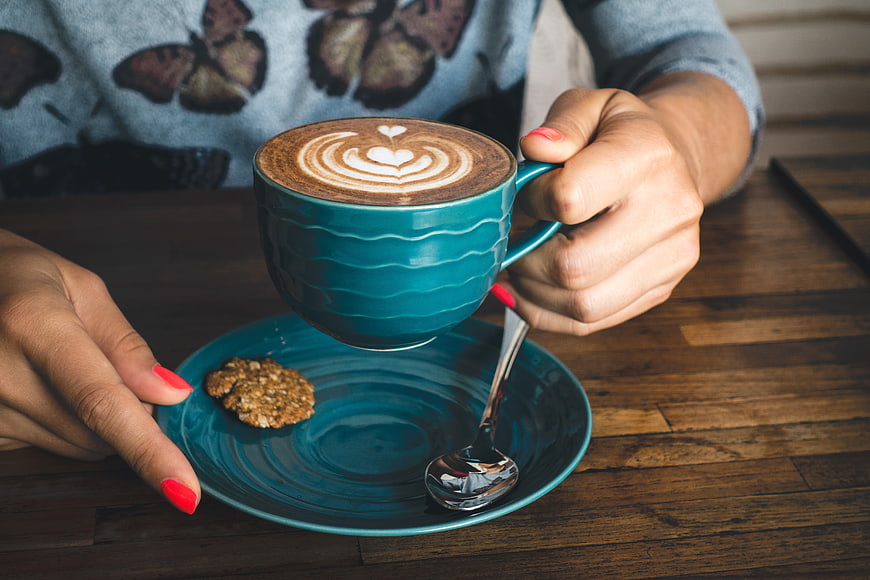 Woman holding teal cup of latte with heart art