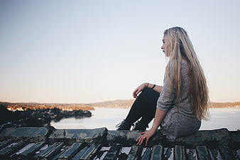 Blonde Woman Sitting on Roof Overlooking Ocean at Sunset