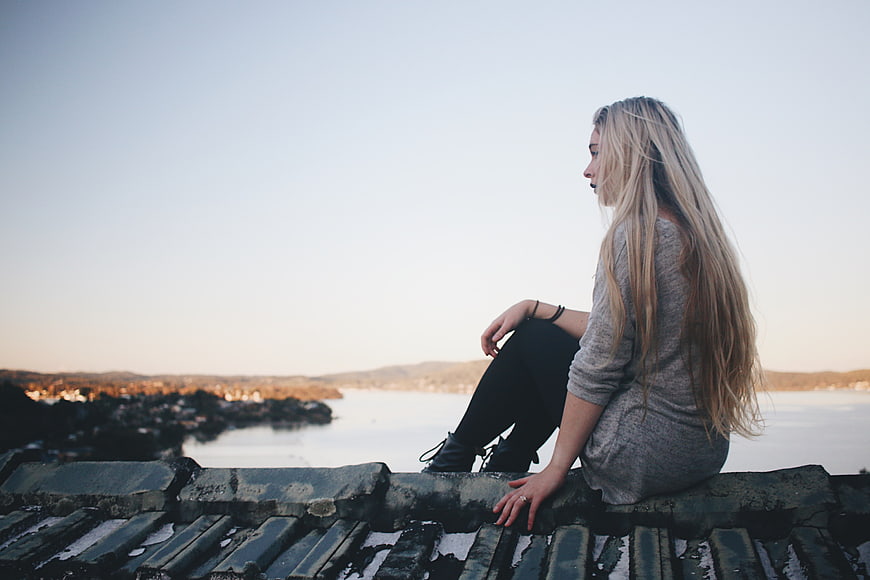 Blonde Woman Sitting on Roof Overlooking Ocean at Sunset