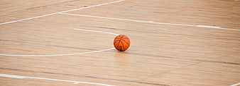 Lone orange basketball on empty hardwood court