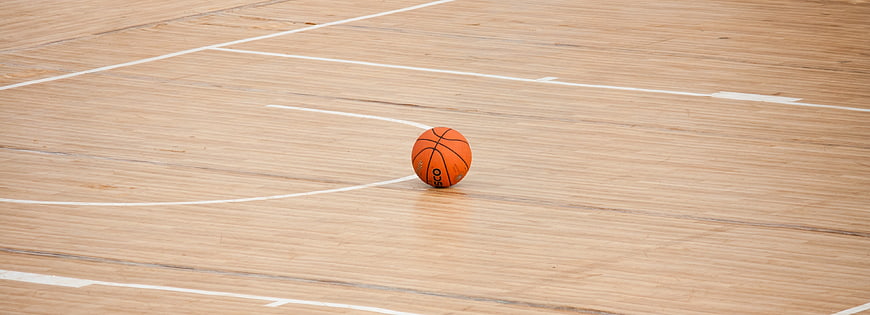 Lone orange basketball on empty hardwood court