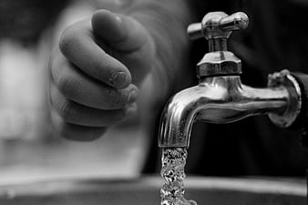 Black and white close-up of a hand reaching for a running water tap