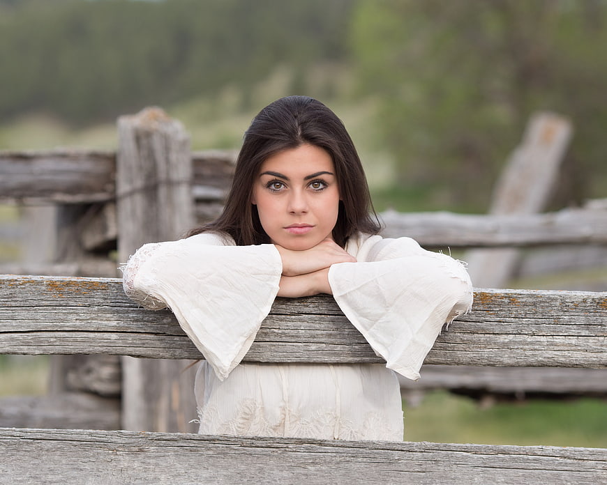 Portrait of Young Brunette Woman Leaning on Rustic Wooden Fence