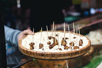 Hand holding wooden platter of fried cheese skewers