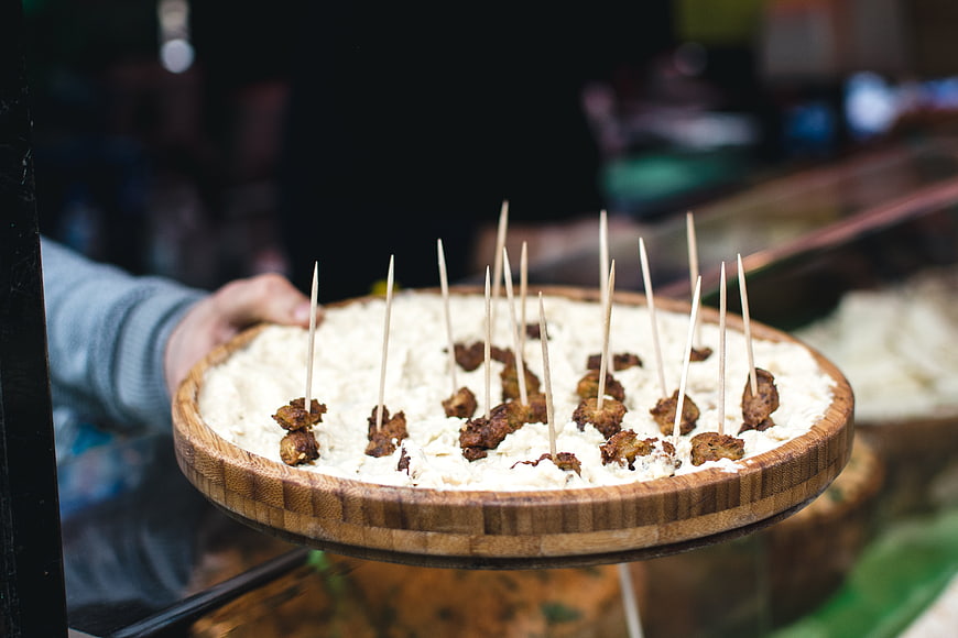 Hand holding wooden platter of fried cheese skewers