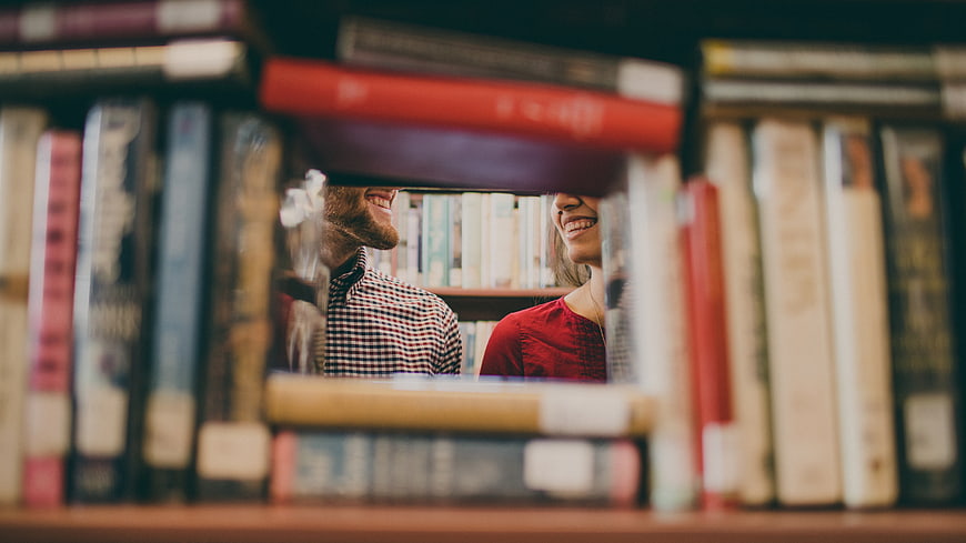 Happy couple smiling through gap in bookshelf