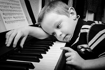 Tired young boy resting head on piano keys