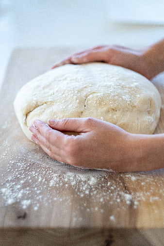 Hands kneading fresh bread dough on wooden board