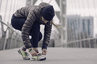 Woman tying running shoes on bridge in winter