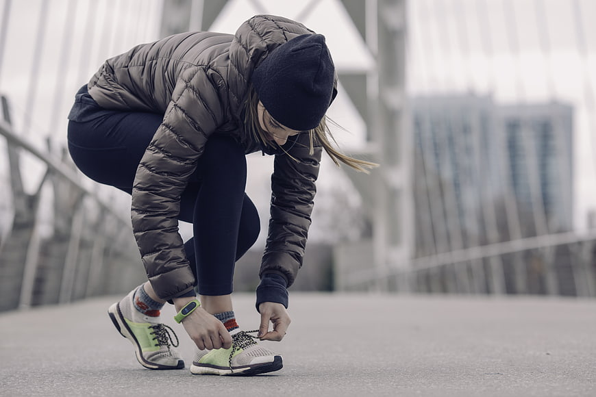 Woman tying running shoes on bridge in winter