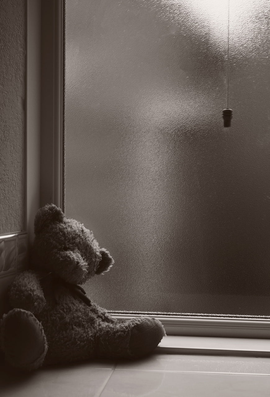 Lonely teddy bear sitting by frosted window