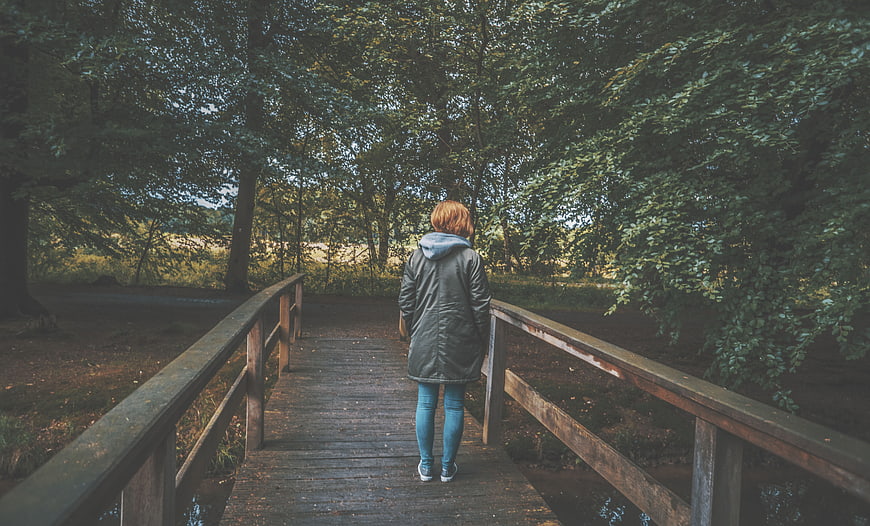 Woman Walking Alone on Wooden Bridge in Forest
