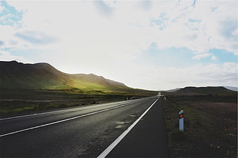 Empty Highway Stretching Through Green Hills Under Cloudy Sky