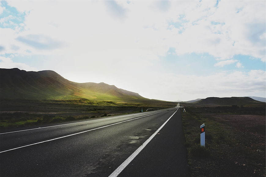 Empty Highway Stretching Through Green Hills Under Cloudy Sky