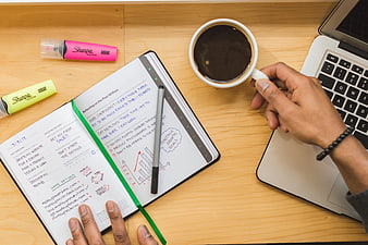 Flat lay of planner, coffee, and laptop on wooden desk