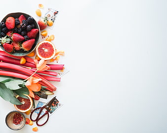 Flat lay of fresh berries, rhubarb, and flowers on white background