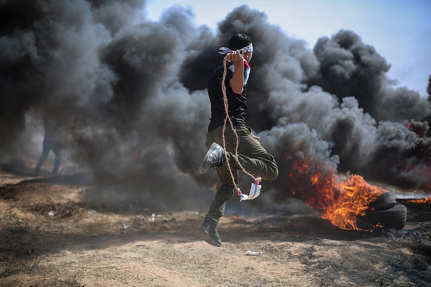 Palestinian man jumping over burning tires in Gaza