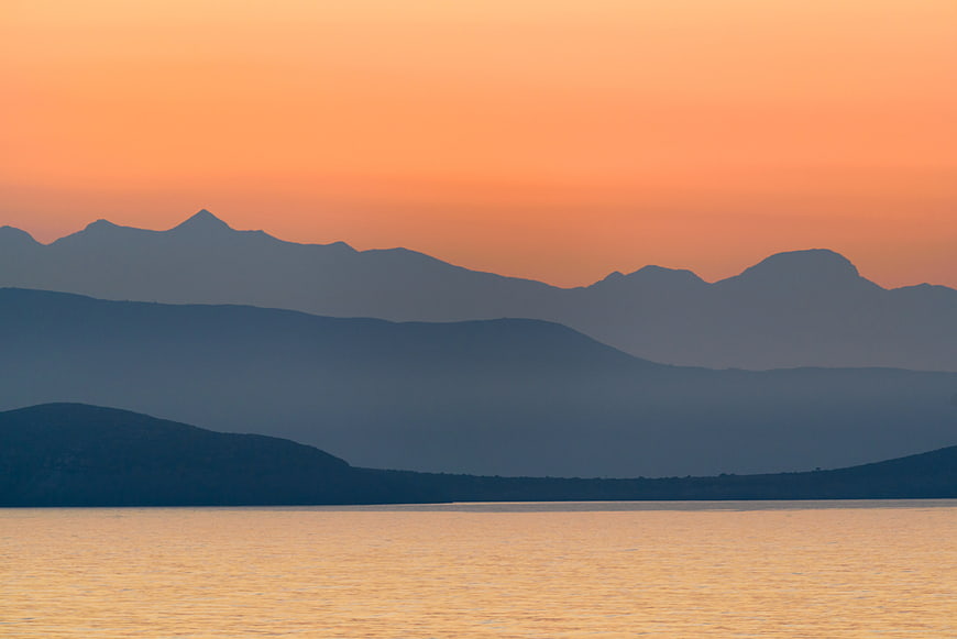 Serene sunset over layered mountains and calm sea