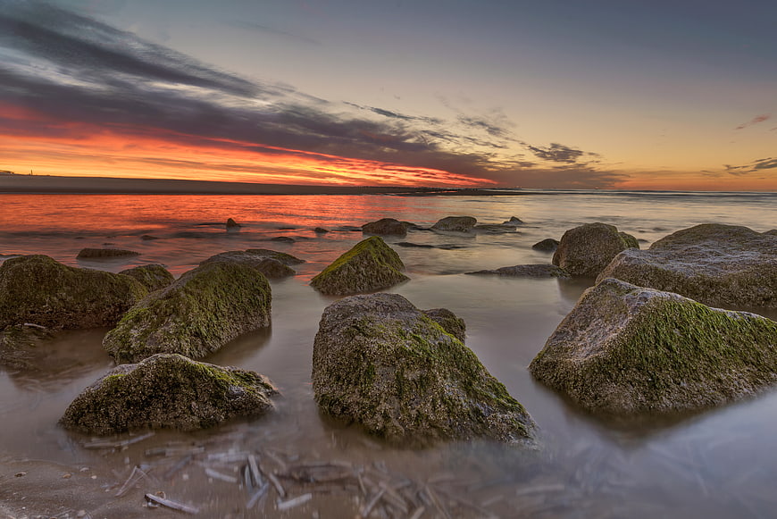 Dramatic Sunset Over Mossy Rocks on Beach