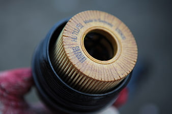 Close-up of a used car engine oil filter held by a gloved hand
