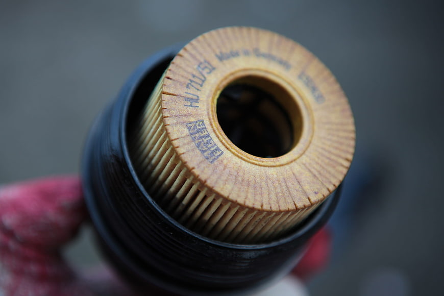 Close-up of a used car engine oil filter held by a gloved hand
