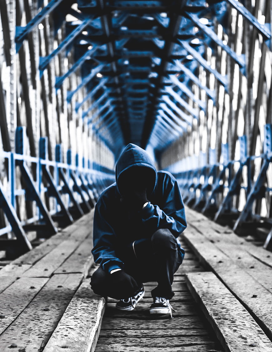 Anonymous hooded figure crouching on wooden bridge