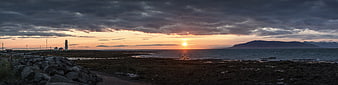 Panoramic Sunset Over Rocky Coastline with Lighthouse and Mountains