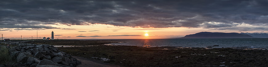 Panoramic Sunset Over Rocky Coastline with Lighthouse and Mountains