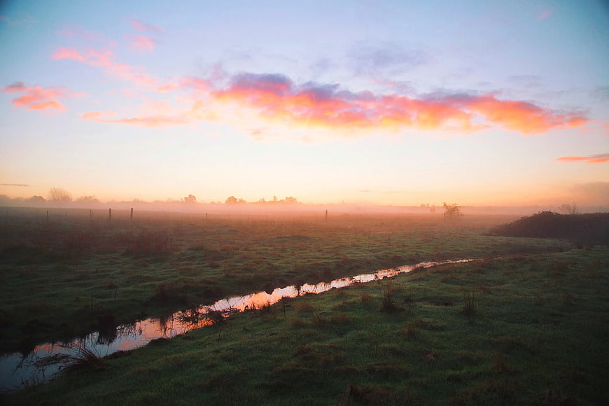 Misty Sunrise Over Green Pasture with Stream
