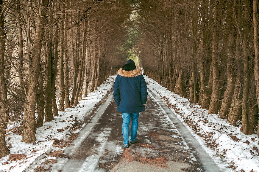 Person walking away on snowy forest road in winter