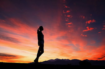 Silhouette of Woman Walking Against Vibrant Sunset Sky