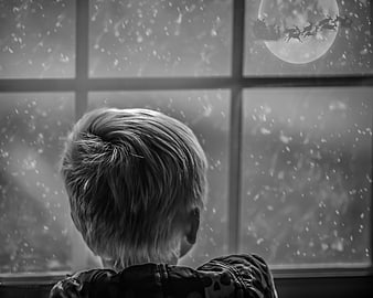 Child watching Santa Claus fly through snowy window