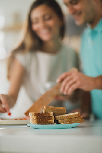 Sliced bread on plate with blurred couple cooking in kitchen