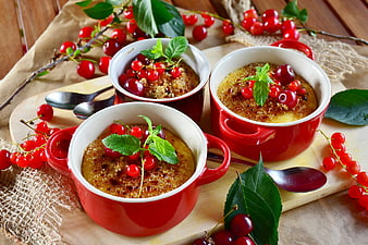 Three red ramekins of creme brulee with fresh cherries and mint
