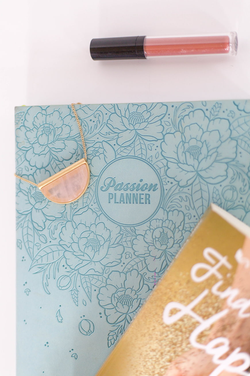 Flat lay of blue floral planner, gold notebook, and lip gloss