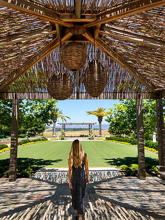 Woman Walking Under Thatched Roof Toward Palm Trees