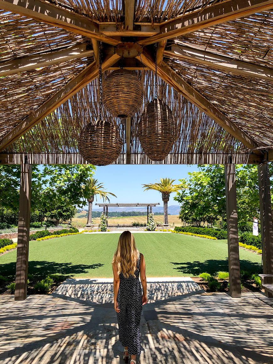 Woman Walking Under Thatched Roof Toward Palm Trees