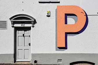 White building facade with large orange letter P mural and grey door